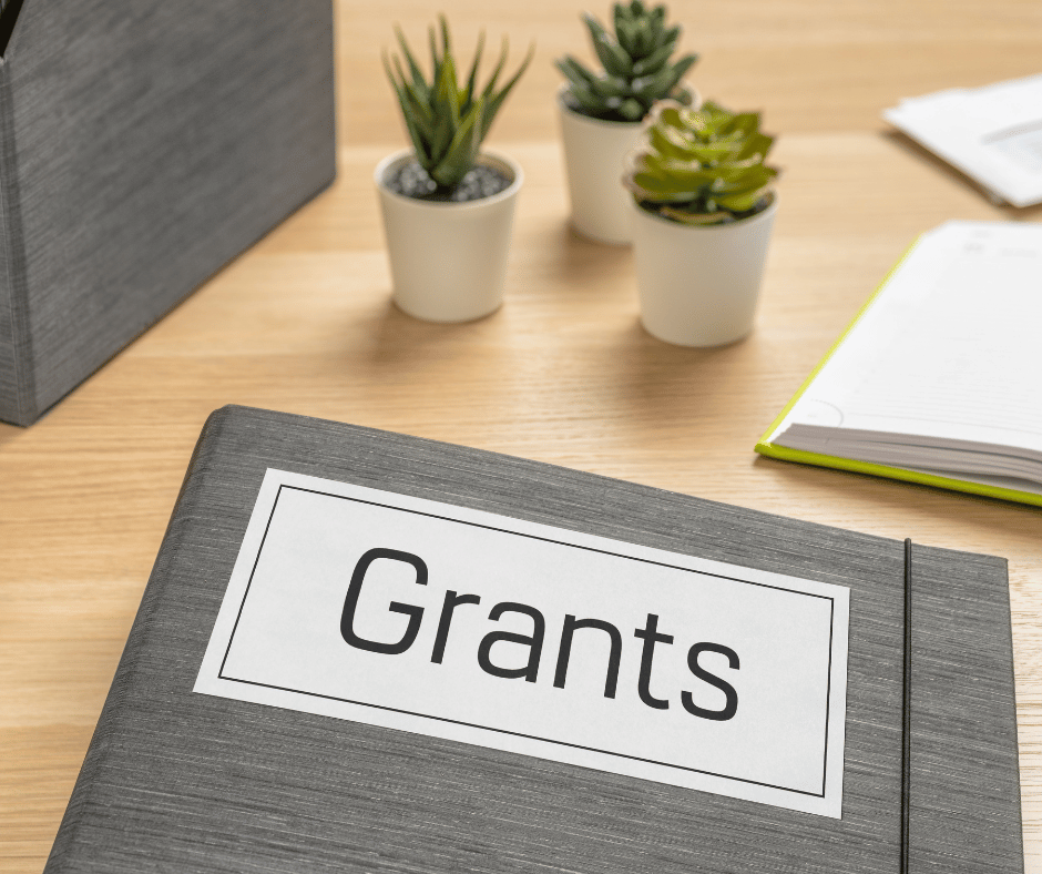 A grey folder with a white label that says grants, on a light wood desk